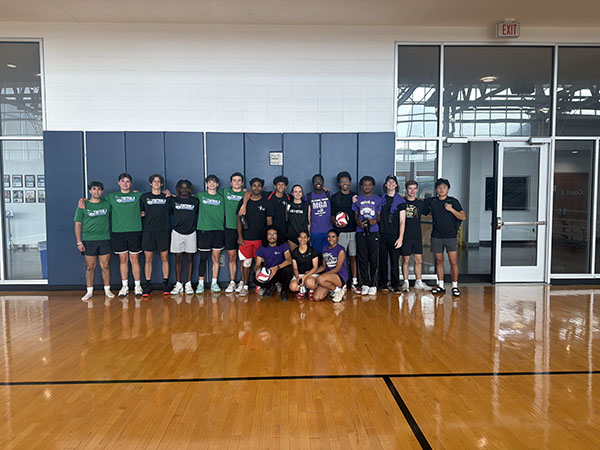 Group photo of MGA and GCSU volleyball club members posing together on an indoor basketball court.